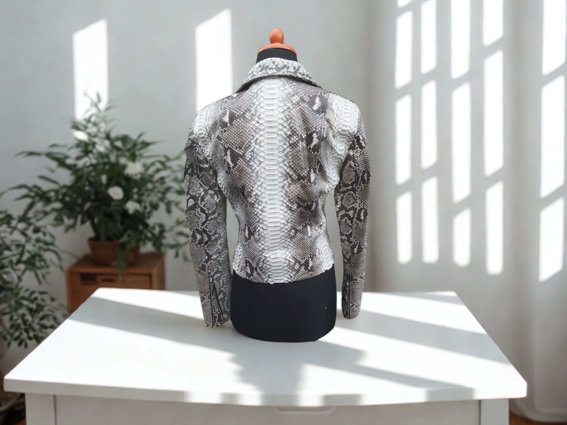 Mannequin wearing a snakeskin jacket on a white table with a light background